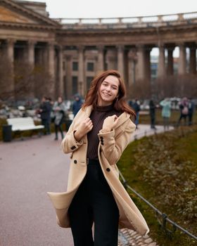Beautiful funny naughty stylish fashionable happy girl dancing on streets of St. Petersburg city. Charming smiling woman with long dark hair, vertical. Autumn, winter