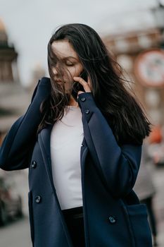 Woman with long hair talking on phone. Autumn or winter, girl in outdoor. Beautiful intelligent brunette in street of Saint-Petersburg in city center, copy space, vertical