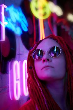 Girl in neon lights at party in nightclub, beautiful woman in sunglasses, with long pink hair, with dreadlocks pigtails, bright and stylish in the glow of neon signs, vertical, close up