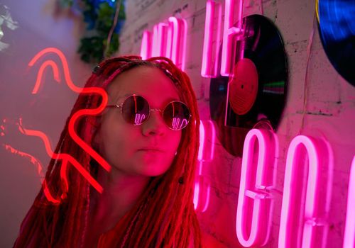 Girl in neon lights at party in nightclub, beautiful woman in sunglasses, with long pink hair, with dreadlocks pigtails, bright and stylish in the glow of neon signs