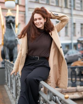 Beautiful serious stylish fashionable smart girl standing on bridge and smiling, St. Petersburg city. Charming thoughtful woman with long dark hair, top shoot, vertical