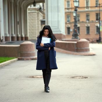 Beautiful serious smart girl brunette student holding notebooks and textbooks, goes walking at University on street of St. Petersburg. A charming woman with long dark hair is studying at a course