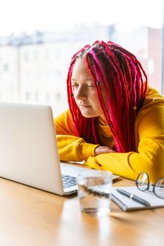 A woman looks at a laptop and squints. The concept of poor vision or a strong concentration on social networks. Girl with long pink hair, designer, creative specialist, freelancer, blogger.