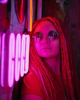 Girl in neon lights at party in nightclub, beautiful woman in sunglasses, with long pink hair, with dreadlocks pigtails, bright and stylish in the glow of neon signs