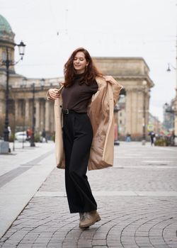 Beautiful funny naughty stylish fashionable happy girl dancing on streets of St. Petersburg city. Charming smiling woman with long dark hair, vertical. Autumn, winter