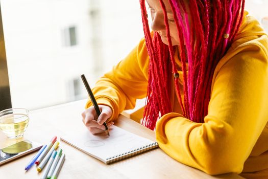 Girl sits in cafe and draws drawing with colored pencils and markers in notebook. Rest and relaxation, hobbies. The remote work concept of designer, illustrator, artist, close up