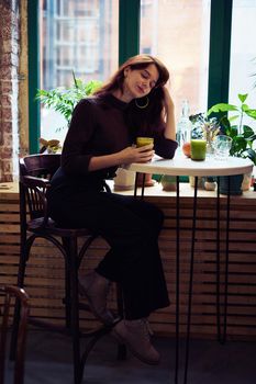 Beautiful serious stylish fashionable smart girl is sitting in a cafe and drinking healthy smoothie or latte vegan. Charming thoughtful woman with long dark brown hair, vertical