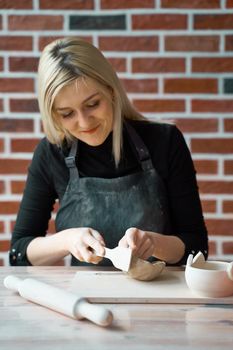 Happy woman making ceramic pottery, tap with spatula. Concept for woman in freelance, business. Handcraft product. Earn extra money, side hustle, turning hobbies into cash and passion into a job