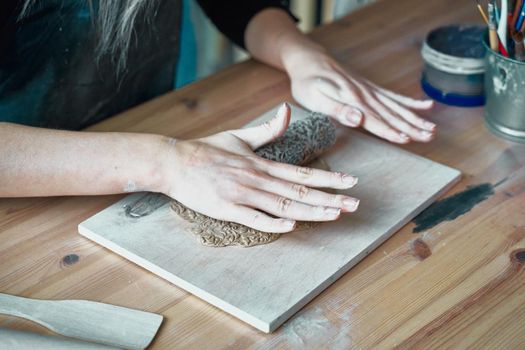 Woman making pattern on ceramic plate, hands close-up, focus on palms with clay and lace. Creative hobby concept, side hustle, turning hobbies into cash, passion into a job