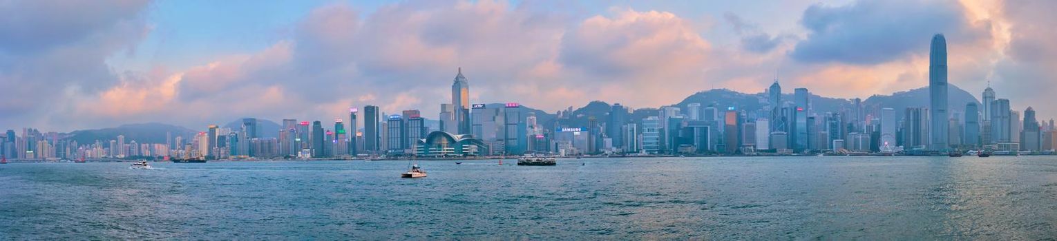 HONG KONG, CHINA - APRIL 28, 2018: Hong Kong skyline cityscape downtown skyscrapers over Victoria Harbour in the evening on sunset with junk tourist boat ferries . Hong Kong, China