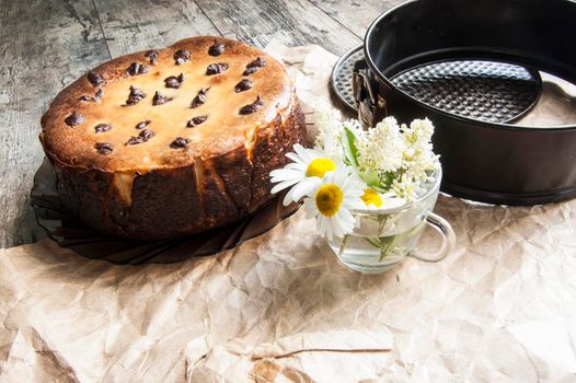 Cheesecake on an old table with a bouquet of daisies and a form for baking. Near wrapping paper. Retro style. From the series "Still Life with cheesecake"