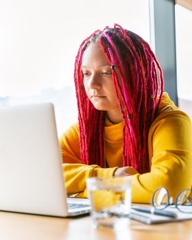 A woman is looking at a laptop. The concept of strong concentration on social networks, immersion in the virtual world. Girl with long pink hair, designer, creative specialist, freelancer, blogger.