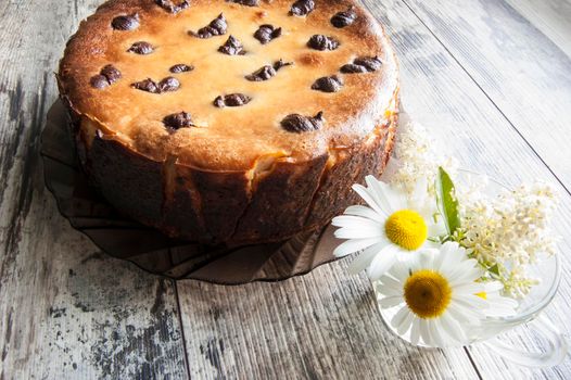 Cheesecake on an old table with a bouquet of daisies and a form for baking. Near wrapping paper. Retro style.From the series "Still Life with cheesecake"