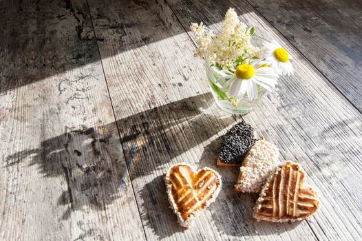 Cookies in the shape of heart on the table. Near a bouquet of daisies. Sunlight plays on an old table. Retro style. From the series "Valentine's Day Cookies"