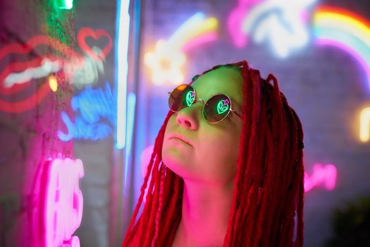 Girl in neon lights at party in nightclub, beautiful woman in sunglasses, with long pink hair, with dreadlocks pigtails, bright and stylish in the glow of neon signs