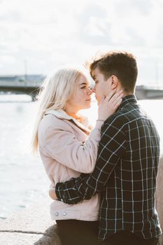 The boy looks tenderly at the girl and wants to kiss. A young couple stands embracing. The concept of teenage love and first kiss, sincere feelings of man and woman. The city, the waterfront. Vertical