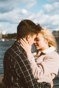 The boy looks tenderly at the girl and wants to kiss. A young couple stands embracing. The concept of teenage love and first kiss, sincere feelings of man and woman. The city, the waterfront.