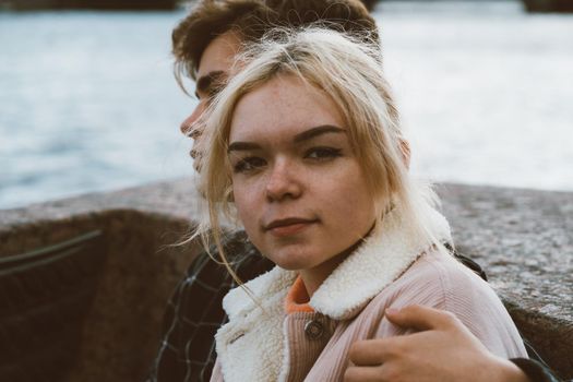 Teenagers in love sit on the waterfront in the city center, resting in the autumn sun. Concept the first teenage love, the beginning of relations. A boy and a girl meet on a date, a couple. Girl close up