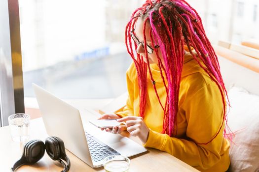 The concept of the work of a writer, journalist, blogger. Remote work, freelance. Bright beautiful young girl with long pink hair is typing on mobile