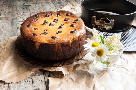 Cheesecake on an old table with a bouquet of daisies and a form for baking. Near wrapping paper. Retro style. From the series "Still Life with cheesecake"