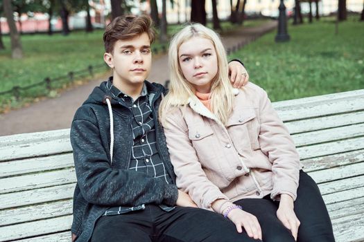 Teenagers in love sit on a park bench in autumn, looking straight ahead. Concept of teen love