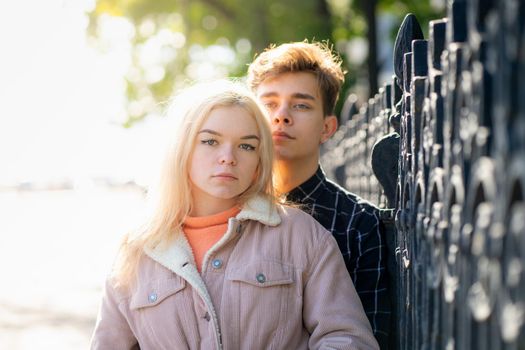 A man gently hugs a woman, a guy and a girl are close to the fence of the Park, looking forward. The concept of first teenage love and first kiss. A boy with dark hair and girl the blonde Scandinavian looks, couple.