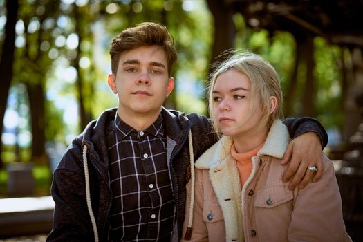 Teenagers in love sit on park bench, resting in the rays of autumn sun, boy looking straight ahead. Concept of teen love