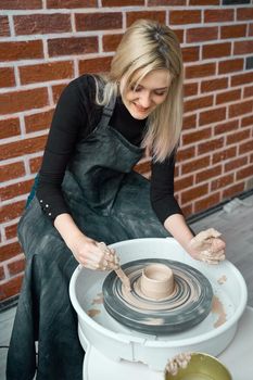 Smiling happy woman making ceramic pottery on wheel. Concept for woman in freelance, business. Handcraft product. Earn extra money, side hustle, turning hobbies into cash and passion into a job