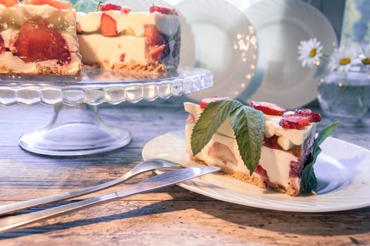 Strawberry cake on a glass base and slice of cake on the white plate with a bouquet of daisies