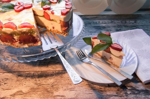 Strawberry cake on a glass base and slice of cake on the white plate with a bouquet of daisies