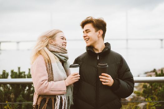 Lovely brunette guy and pretty girl blonde drink coffee and talking on a date. Loving teenagers are happy, smiling, laughing. Teen Love Concept. Outdoor.