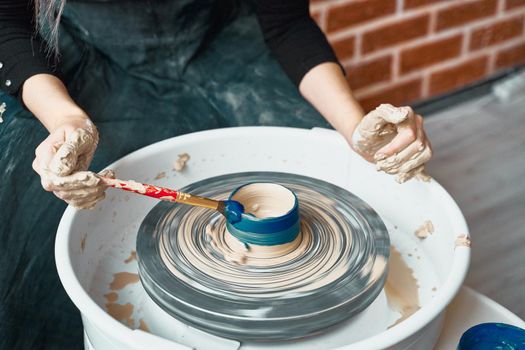 Unrecognisable woman making ceramic pottery on wheel, paints blue. Concept for woman in freelance, business. Handcraft product. Earn extra money, side hustle, turning hobbies into cash, close up
