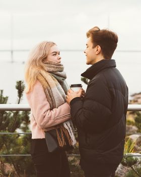 Lovely brunette guy and pretty girl blonde drink coffee and talking on a date. Loving teenagers are happy, smiling, laughing. Teen Love Concept. Outdoor.