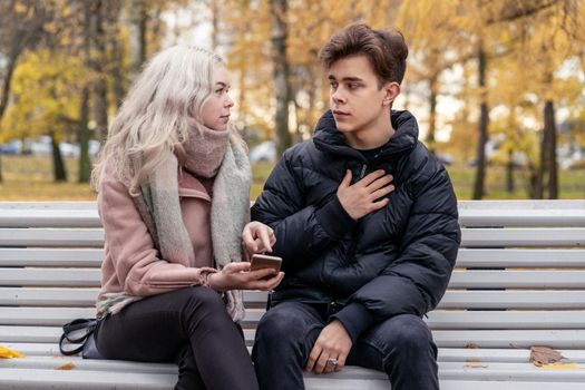 Young beautiful blonde girl blames her boyfriend by pointing finger to the phone screen. The concept of jealousy, quarrels, difficulties in communicating through social networks