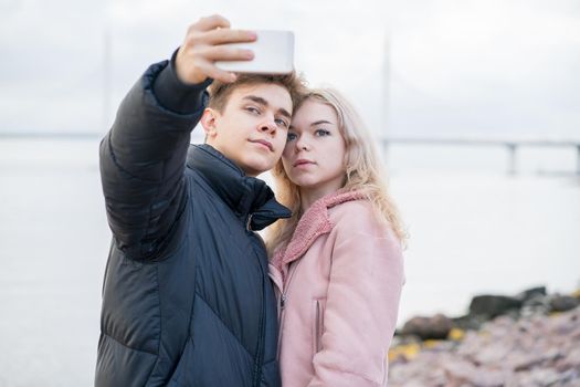 Loving teenagers on date. Cute brunette boy and beautiful blonde girl take a selfie on a cell phone. Concept of teen love, millennium generation