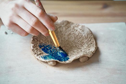 Unrecognised Woman making pattern on ceramic plate, hands close-up, focus on palms with paint brush. Creative hobby concept. Earn extra money, side hustle, turning hobbies into cash, passion into a job