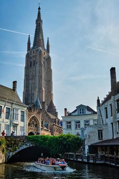 BRUGES, BELGIUM - MAY 28, 2018: Tourist boat with tourists in canal near Church of Our Lady . Brugge Bruges, Belgium