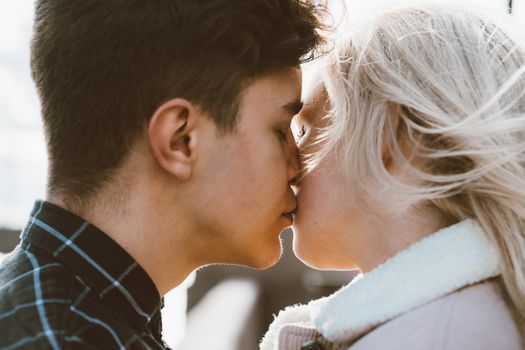 The boy looks tenderly at the girl and wants to kiss. A young couple stands embracing. The concept of teenage love and first kiss, sincere feelings of man and woman. The city, the waterfront. Close up