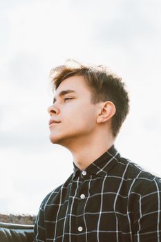 Portrait of a young guy, brunette with dark hair, Caucasian. Close - up of a guy, boy, man looking past camera. Outdoor in city by water. Bottom to top view