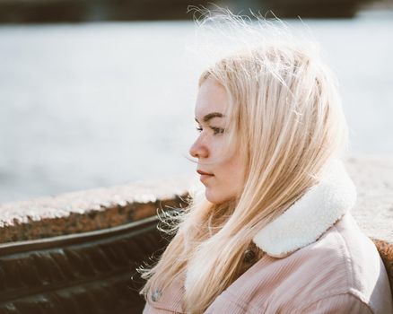 Portrait of a young girl, blonde with bleached hair, Caucasian. Scandinavian style. Close - up of a teenage woman looking past a camera in the city near the water.
