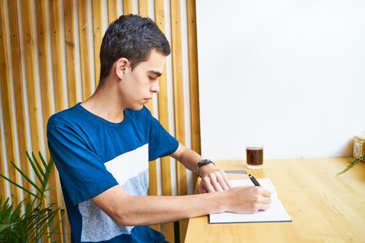 Young man writing information to notepad, teenager in casual clothes plans a schedule, copy space