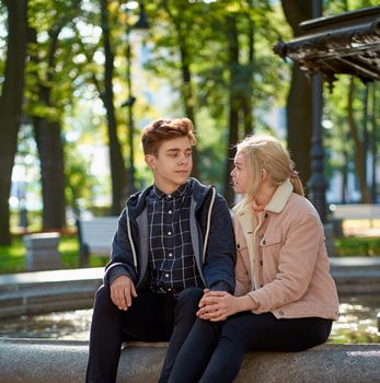 Lovers boy and girl look at each other, sitting in the Park near the fountain in the fall. Girlfriend and Boyfriend are talking concept of love and happiness, side view