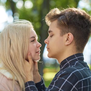 The boy looks tenderly at the girl, hands clasped her face and wants to kiss. Concept of teenage love and first kiss