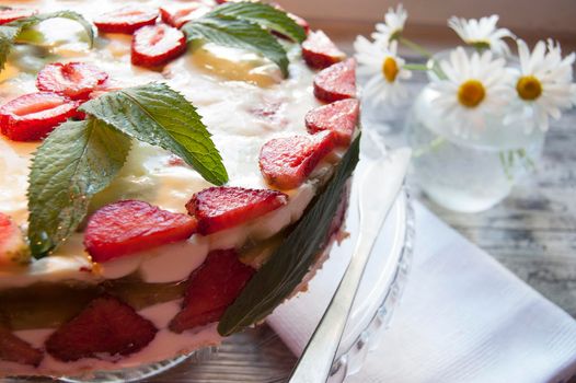 Strawberry cake on a glass base with a bouquet of daisies