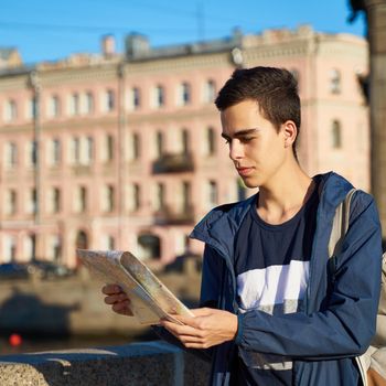 young man standing on the street of a big city and looking at a guide, a tourist in St. Petersburg got lost his way