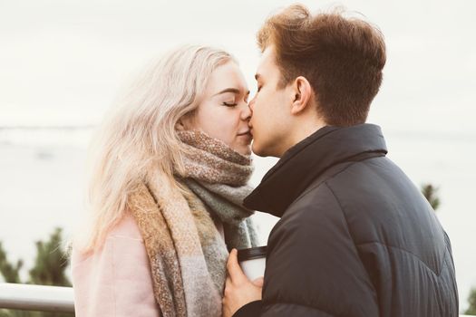 Lovely brunette guy and pretty girl blonde drink coffee and talking on a date. Loving teenagers are happy, smiling, kissing. Teen Love Concept. Outdoor. Close up portrait