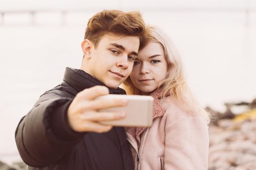 Loving teenagers on date. Cute brunette boy and beautiful blonde girl take a selfie on a cell phone. Concept of teen love, close up
