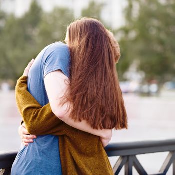 Girl with long thick dark hear embracing redhead boy on bridge, teen love at sunset, summer time