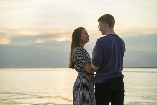 teen couple, ocean clouds and sunset on background, girl looking at boy and smiling