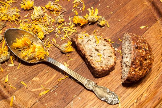 A few slices of bread, a teaspoon and dried marigold flowers on a wooden cutting board.